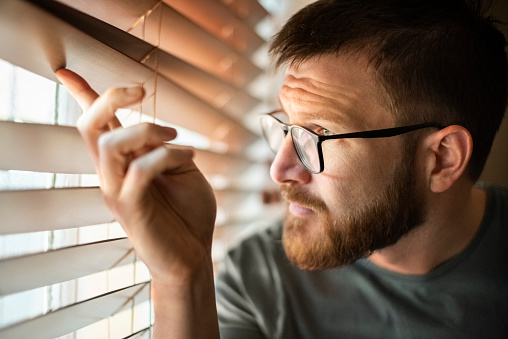 Close-up of a man looking outside through window blinds