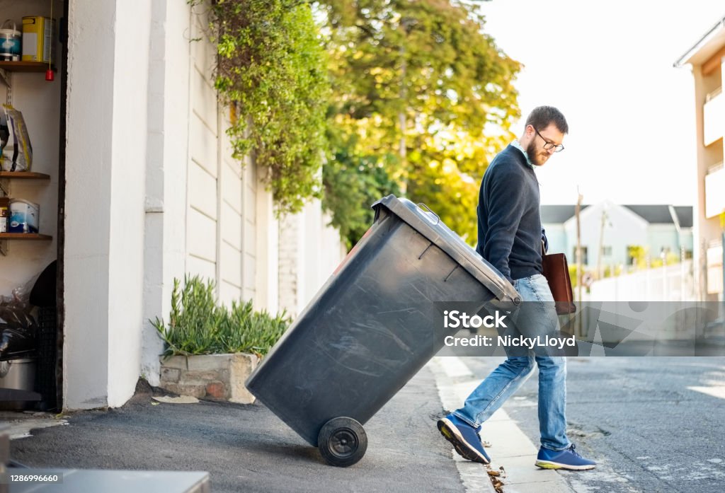 Hauling garbage Man pulling a wheeled dumpster out of his garage while going to work Garbage Stock Photo