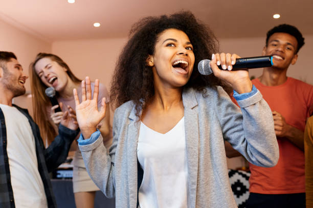 istock Sing on. Pretty mixed race girl looking happy while holding microphone and singing at karaoke party with best friends. Happy multicultural people spending time together 1287000337