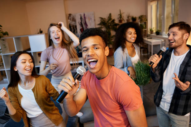 istock Radiate fun. Enthusiastic young guy singing with microphone while playing karaoke with friends in the modern apartment, having home party 1287000362