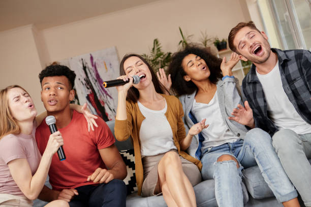 istock Sing as you can. Enthusiastic group of friends singing with microphone while playing karaoke at home, sitting on the couch at home 1287000395