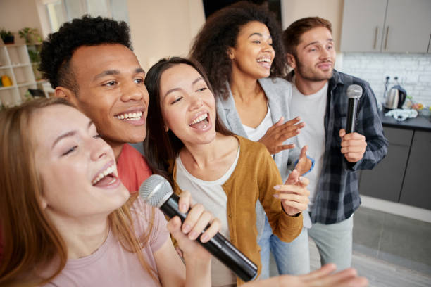 istock Music for life. Happy multicultured friends singing with microphone while playing karaoke at home, standing in the modern apartment 1287000461