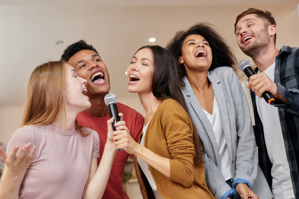 istock Singing for everyone. Cheerful multicultured friends singing with microphone while playing karaoke at home, standing indoors 1287000465