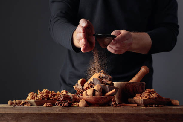 Man sprinkles the chocolates with cocoa powder. On an old wooden table candy, ingredients, and pieces of broken black chocolate. Copy space.