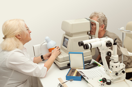 Doctor ophthalmologist checks the eyesight of an senior man patient on modern refractometer
