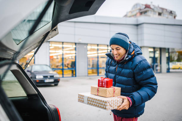 istock Smiling young man holding presents loading his car trunk. Consumerism / shopping concept. Special occasion / holiday shopping concept. 1287007895