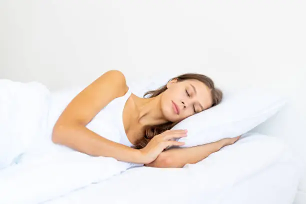 Side view waist portrait of beautiful sleeping woman in bed. Female with long hair resting, good night sleep concept, enjoying fresh soft bedding linen and mattress in bedroom