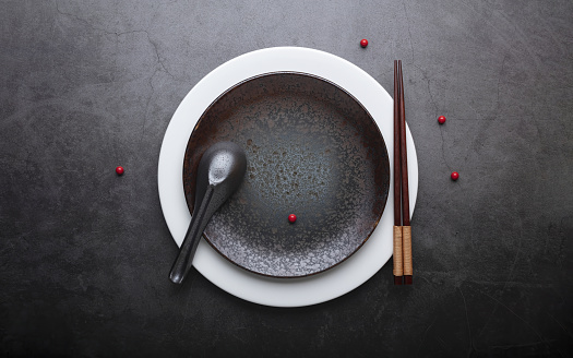 Empty ceramic dish(plate) and chopstick and spoon on grey stone background. Flat lay