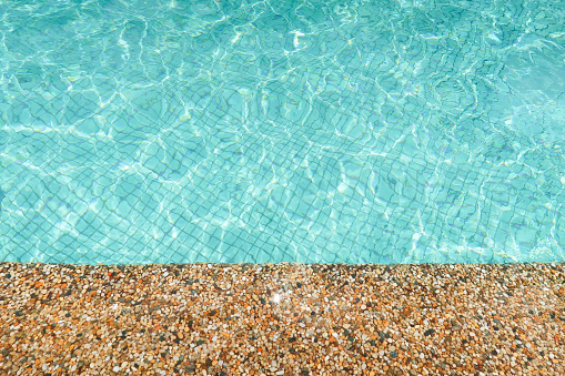 Stone edge of a swimming pool with turquoise shiny  water with sun reflection