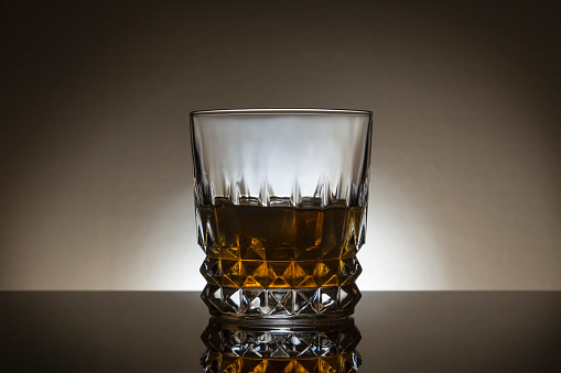 Back lited Whiskey glass on a dark background with reflection in front of the glass.