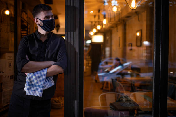 The waiter is waiting for the guests at the door The waiter is waiting for the guests at the door of restaurant. He is wearing protective face mask during pandemic. indoors restaurant hotel work tool stock pictures, royalty-free photos & images