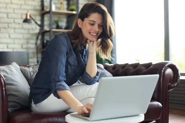 istock Smiling young woman sitting on sofa with laptop computer and chating with friends. 1287025462