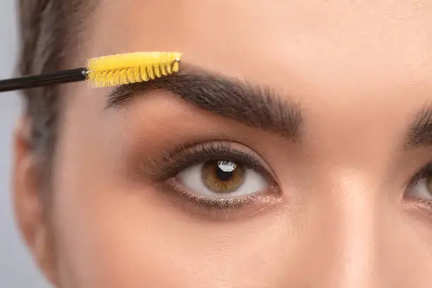 Photo of Makeup artist combs eyebrows with a brush after dyeing in a beauty salon.Professional makeup and cosmetology skin care.