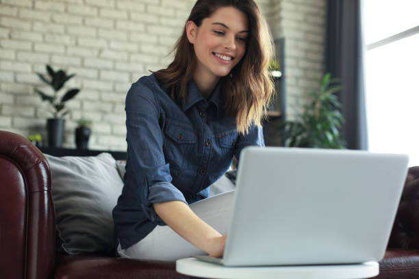 istock Smiling young woman sitting on sofa with laptop computer and chating with friends. 1287025558
