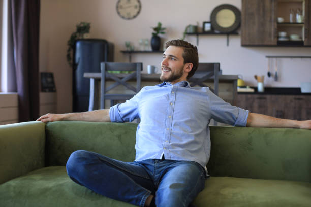 istock Handsome young business man is looking relaxed while sitting on the couch at home. 1287028394