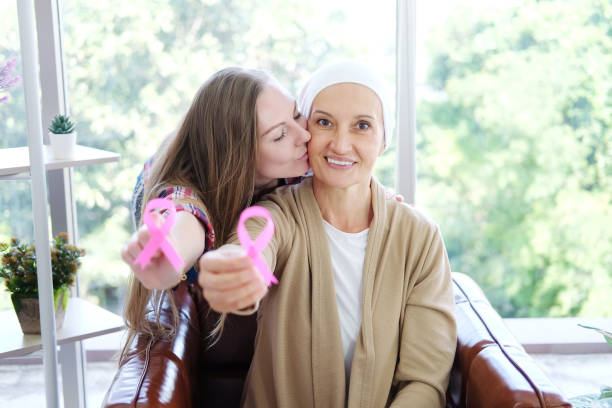 кавказская дочь целует пожилую мать в белый платок улыбается и проведение осведомленн�ости розовая лента общего рака является символом раз - breast cancer pink ribbon alertness стоковые фото и изображения