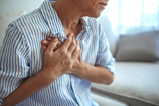 Senior Woman Suffering From Chest Pain While Sitting on Sofa at Home. Portrait of Elderly Woman Having Heart Attack. Heart problems can affect anyone at any time