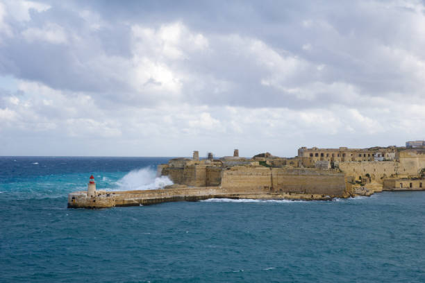 vista do forte st. elmo para o ricasoli grand harbour east breakwater e farol vermelho durante ondas fortes - st elmo - fotografias e filmes do acervo