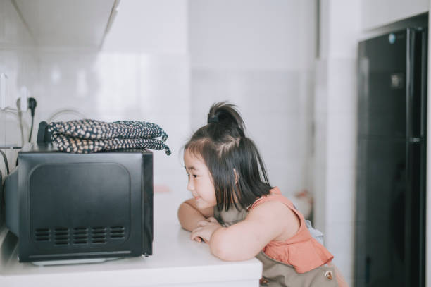young asian chinese girl waiting and looking her food out from microwave using protective glove in  kitchen young asian chinese girl waiting and looking her food out from microwave using protective glove in  kitchen inside microwave stock pictures, royalty-free photos & images