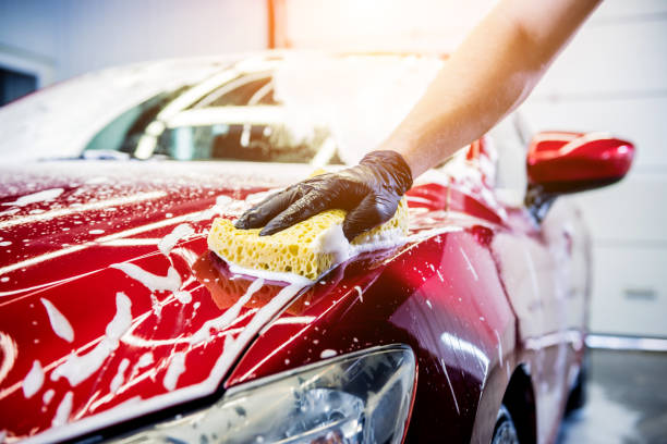 arbeiter waschen rotes auto mit schwamm auf einer autowäsche - seife fotos stock-fotos und bilder