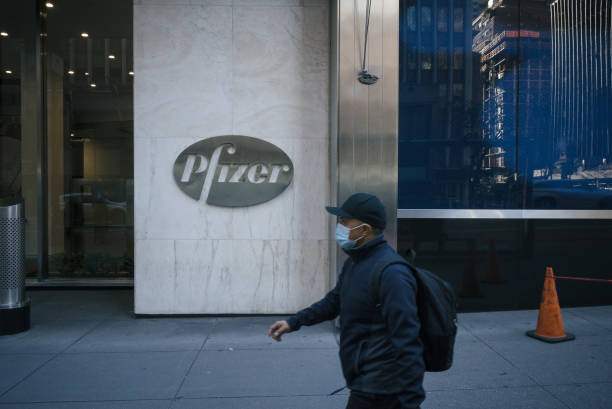 New York during the COVID-19 emergency. Manhattan, New York. November 20, 2020. A man wearing a mask walks by Pfizer logo outside the company headquarter on 42nd street. 42nd street stock pictures, royalty-free photos & images