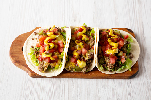 Homemade Cheeseburger Tacos on a rustic wooden board on a white wooden background, low angle view.