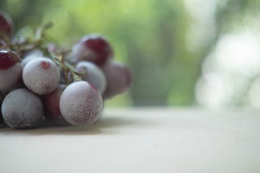 A cluster of red seedless grapes chilled on wood table. Close up with shallow depth of field and selective focus, copy space