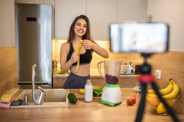 istock Young woman in kitchen recording video on camera. 1287047683