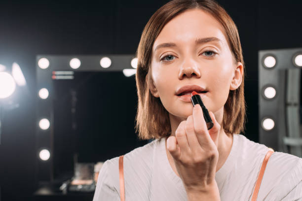 istock Attractive woman looking at camera while applying red lipstick in photo studio 1287050534