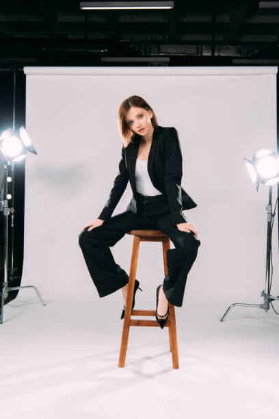 istock Elegant model in formal wear looking at camera while sitting on chair in photo studio 1287050559