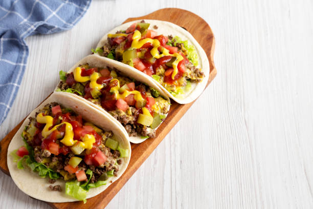 istock Homemade Cheeseburger Tacos on a rustic wooden board on a white wooden surface, low angle view. Space for text. 1287050923