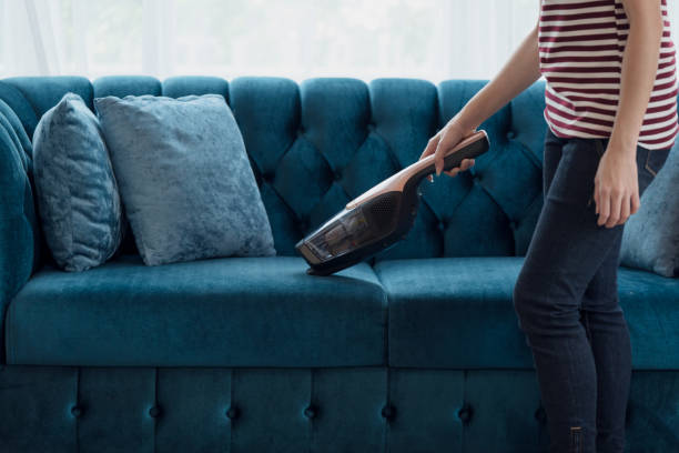Woman housewife vacuuming furniture in a house with a hand-held portable vacuum cleaner Close up of A woman housewife vacuuming furniture in a house with a hand-held portable vacuum cleaner cordless phone stock pictures, royalty-free photos & images