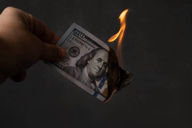 istock Fingers hold a burning 100 USD banknote 1287053348