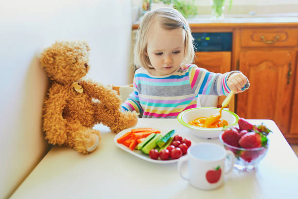 очаровательный малыш девушка ест свежие фрукты и овощи на обед - baby carrot snack healthy eating small стоковые фото и изображения