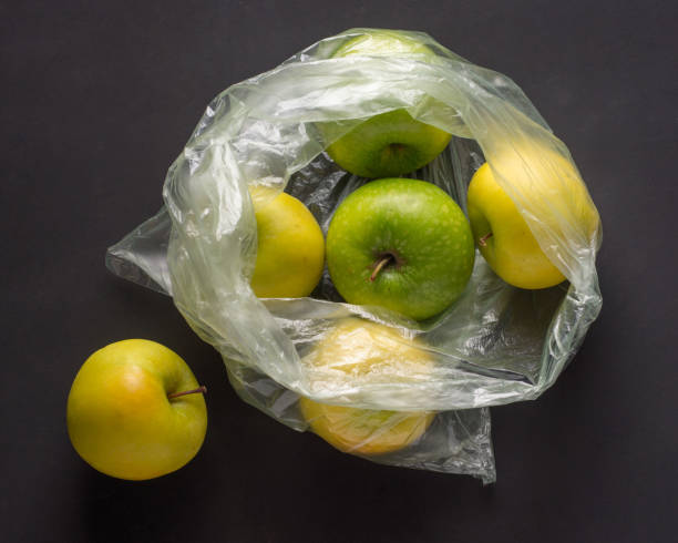 istock single use plastic packaging issue. green apples in plastic bags  on a dark background 1287064719
