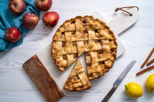 American apple pie on cutting board with ingredients on white wooden board table