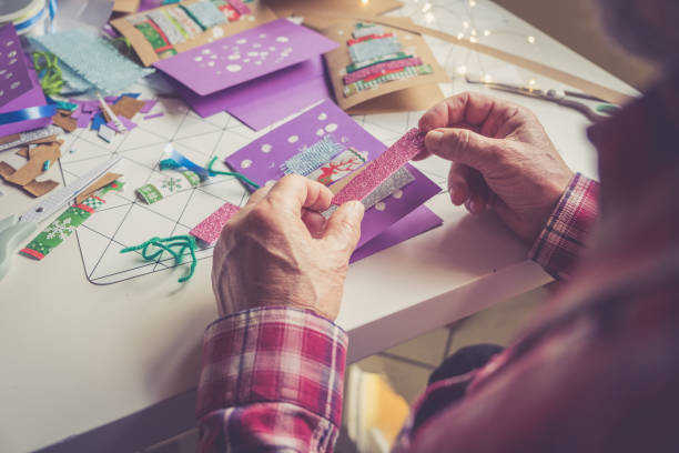 uomo anziano che crea la cartolina di natale a casa - card making foto e immagini stock