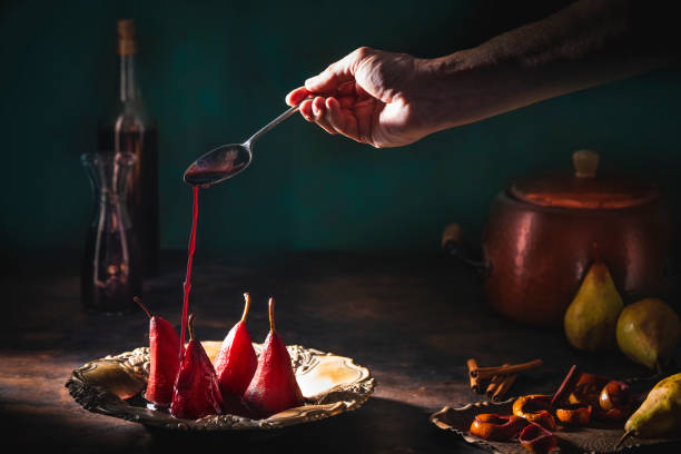 Poached pears in red wine recipe pouring wine on pears with cinnamon and citrus peel with ingredients moody low key dark