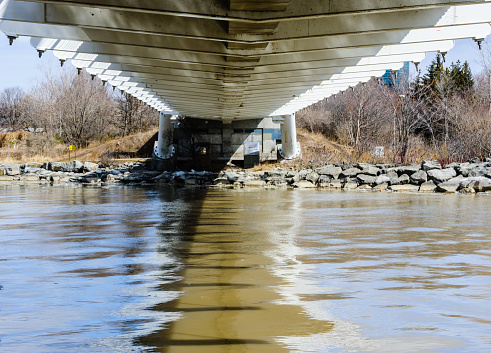 Underneath small metal bridge girders crossing muddy river, in Toronto, Canada.