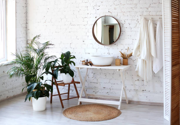 Bathroom interior with big round mirror, table and plants near brick wall