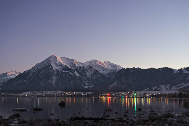 lago thun e a montanha niesen durante o crepúsculo com reflexo de pequenas luzes da aldeia no lago. - lake thun switzerland night lake - fotografias e filmes do acervo