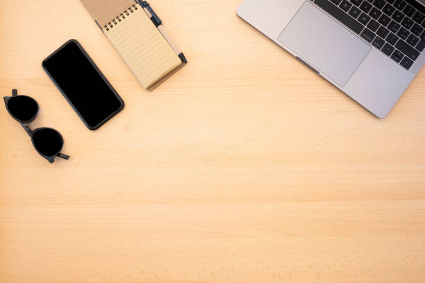 istock Flat lay with copy space, working from home concept during the Covid-19 pandemic. A smart phone, sunglasses, a laptop and a notepad are arranged on a wooden table. 1287086737