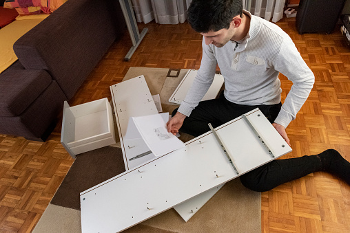Young man reading the instructions to assemble furniture