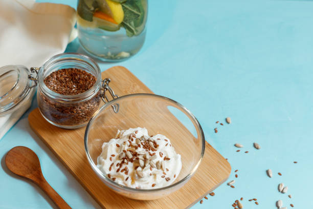Yogurt with flax and sunflower seeds in a glass bowl on a wooden Board and a jar with flax seeds close up with space stock photo