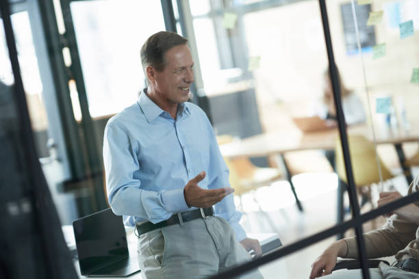 istock Successful mature businessman gesturing and smiling while discussing something with colleagues in the modern office, having a meeting with team 1287095654