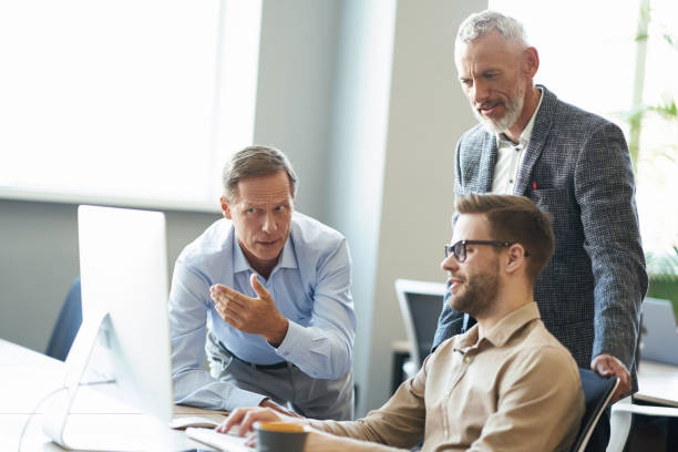 istock Working together. Three businessman looking at computer monitor and discussing something while sitting in the modern office 1287096284