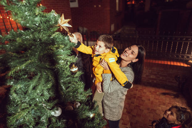istock Young mother decorating christmas tree in front yard with her kids at night 1287096553