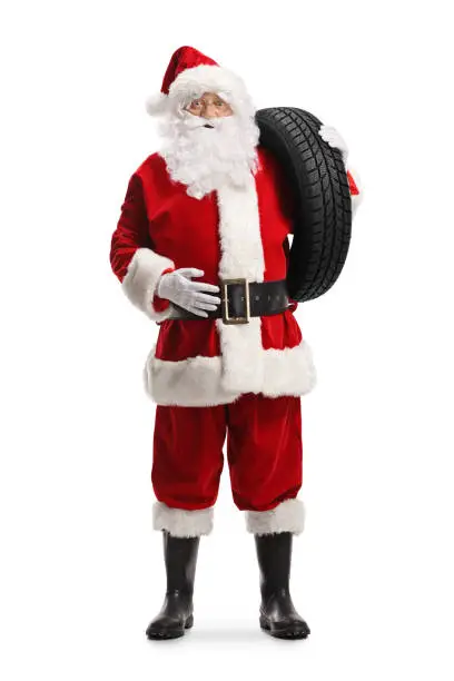 Full length portrait of santa claus carrying a car tire on his shoulder isolated on white background