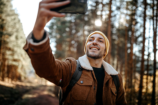 Young man taking selfie while hiking in nature alone on beautiful autumn day