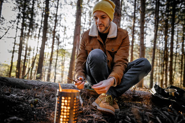 istock Young man igniting fire to warm himself up while relaxing in forest on autumn day 1287100622